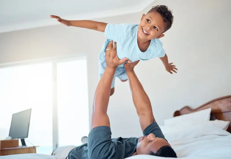 Father lifting son up in air on top of bed